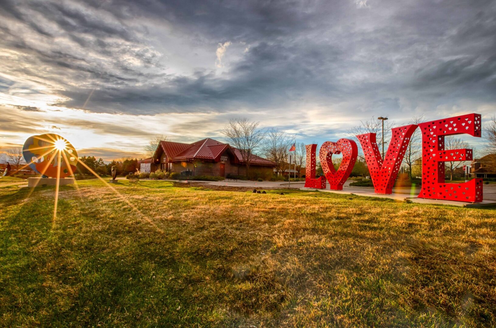 Giant red LOVE sculpture on grass at sunset